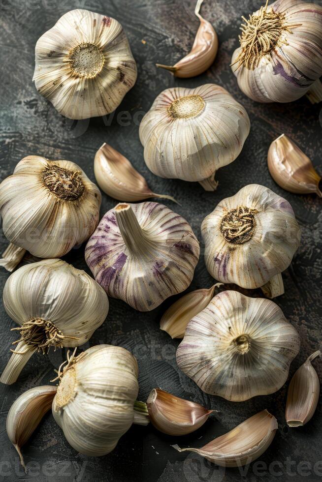 Various garlic cloves and bulbs are spread across a dark table, showcasing their unique shapes and rich textures in an inviting layout photo