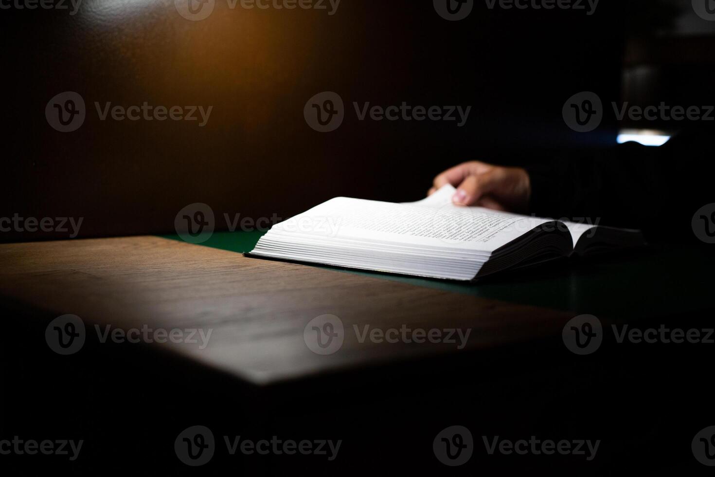 Person holding open book in dimly lit environment, perfect for emphasizing the power of reading and learning in solitude. The image reflects focus, reflection, and intellectual engagement photo