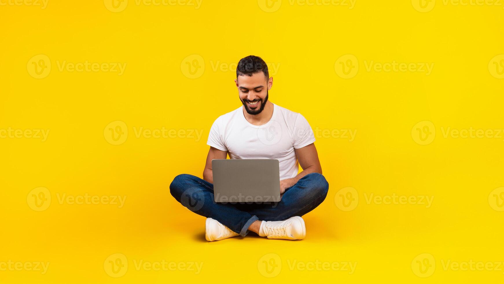 Middle-Eastern Family Using Different Gadgets Browsing Internet On Laptop, Tablet Computer And Smartphone Sitting Over Yellow Studio Background. People And Technology Concept photo