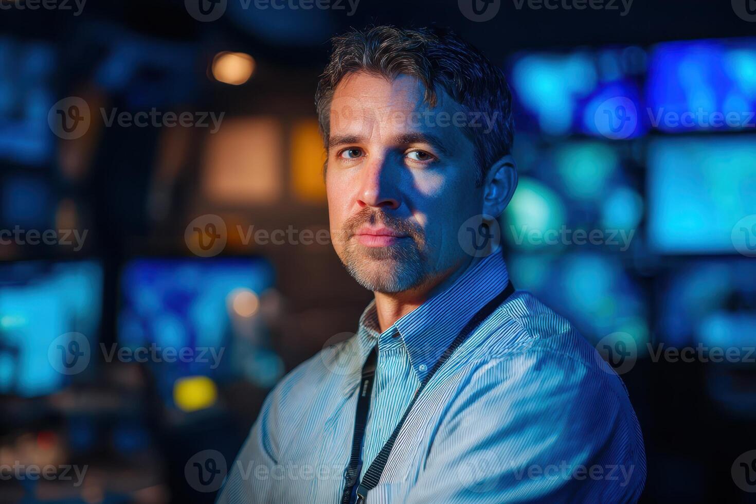 Male figure in a blue shirt is illuminated by bluish light, standing confidently in a control or server room. Monitors with abstract patterns create a high-tech, futuristic vibe photo