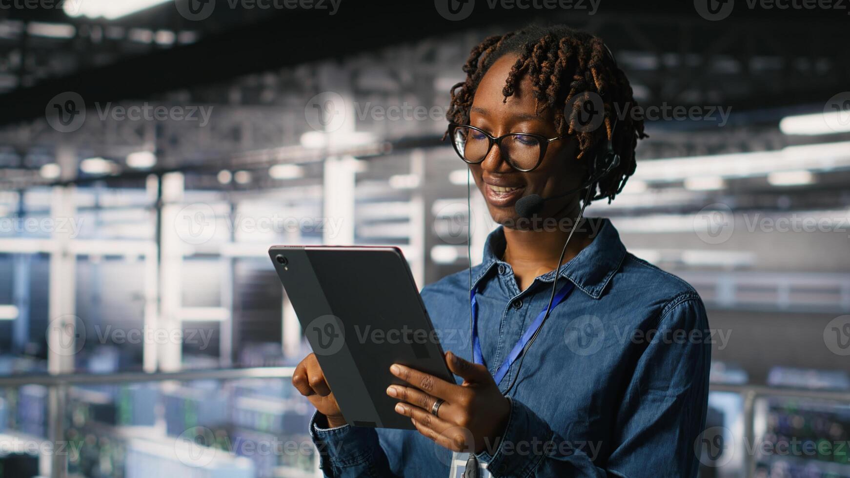 Data center engineer wearing headset microphone providing remote diagnostics using tablet. Technician monitors system health and guides users through infrastructure troubleshooting steps photo