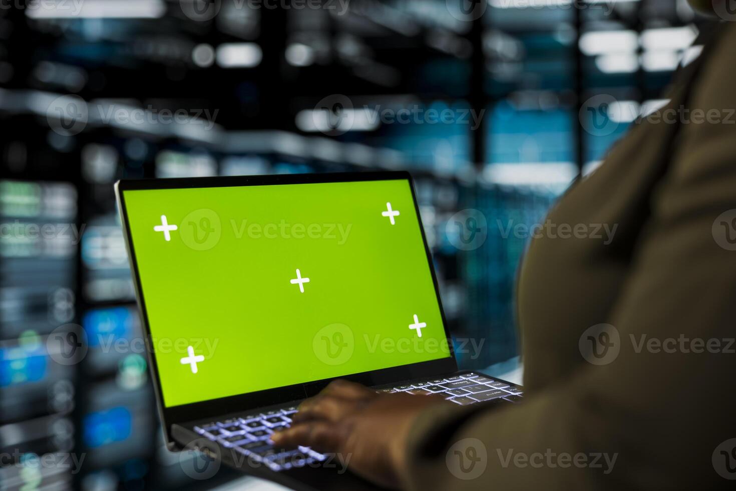 Programmer uses green screen mockup laptop to do maintenance in data center with setup helping companies stay connected. Worker walks with chroma key notebook between server hub rigs blinking lights photo