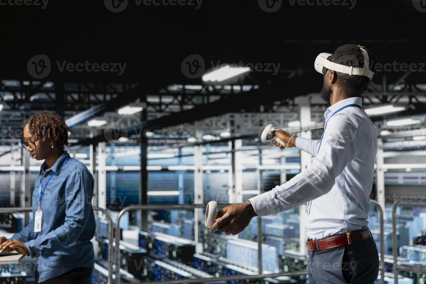 African american AI technician uses VR glasses in server hub to update data security, configuring tech equipment with software tools. Engineer reviewing hardware with virtual reality. photo