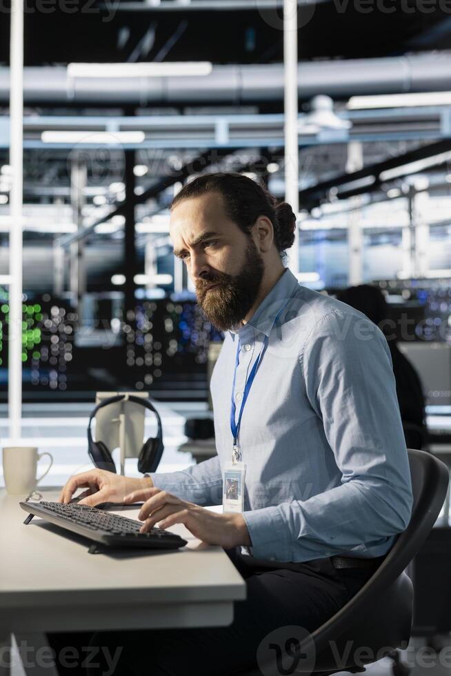 Annoyed engineer in data center frowning at PC monitor after detecting unexpected network outage. Upset server room employee analyzing system logs to determine cause of infrastructure failure photo
