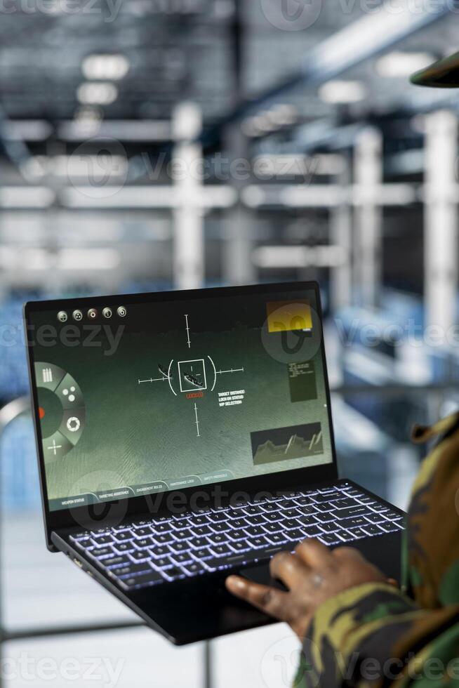 Close up of military technician in data center monitoring warfare drone telemetry on laptop dashboard. IT specialist in server room using tactical interface on notebook to support aerial operations photo