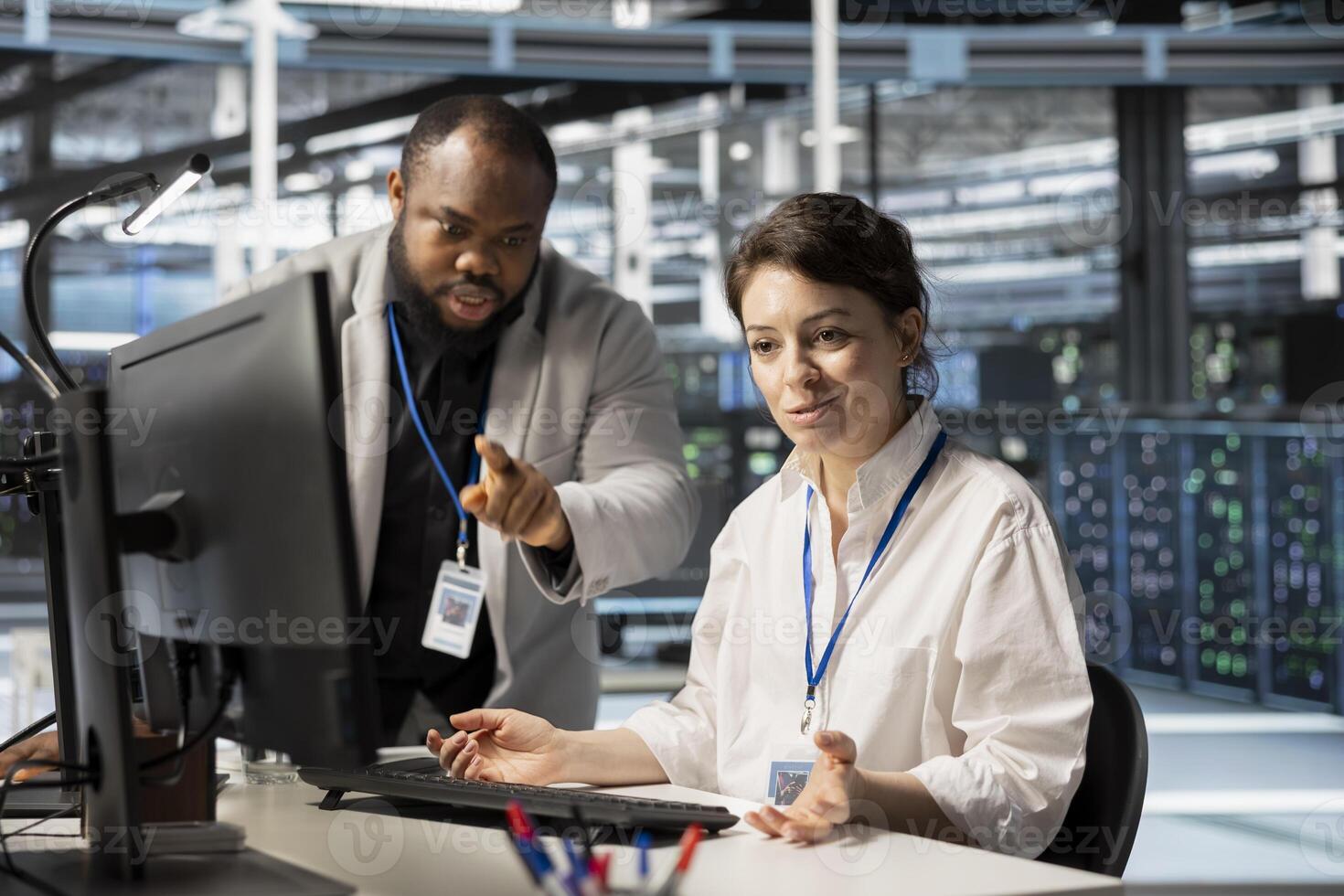 Data center manager supervising work done by engineer updating servers tech, configuring gear using software. Server hub supervisor overseeing worker reviewing hardware analytics photo