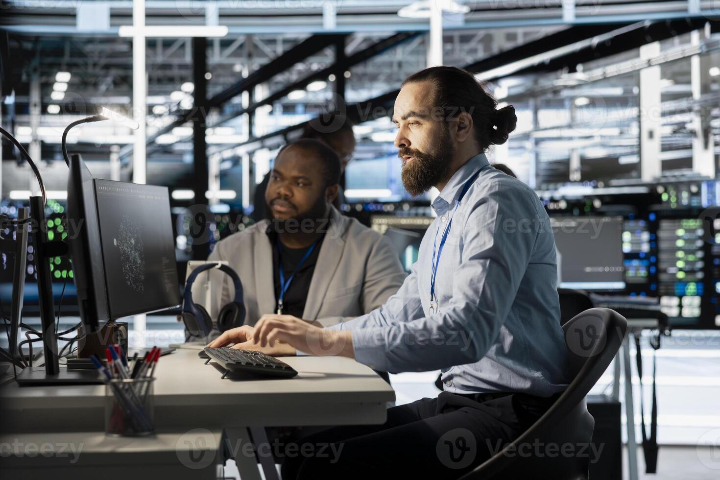 Team of programmers using computer in server farm, analyzing data. Men working in data center office examining infrastructure using device, ensuring system integrity and security photo