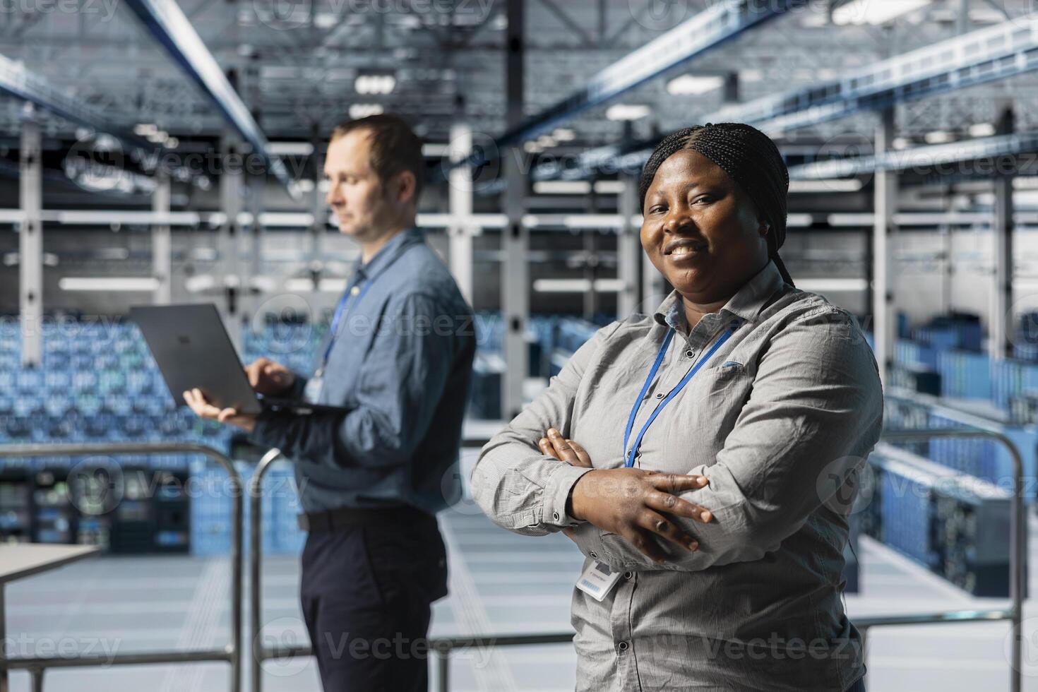 Portrait of smiling server room engineer next to coworker troubleshooting errors using software on laptop. Cheerful african american woman in data center and colleague fixing bugs using notebook photo