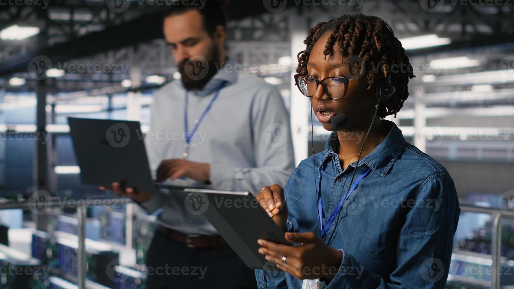 Server room admin using tablet and headset microphone to provide infrastructure tech support. Data center IT specialist resolves backend issues while coordinating with remote teams photo