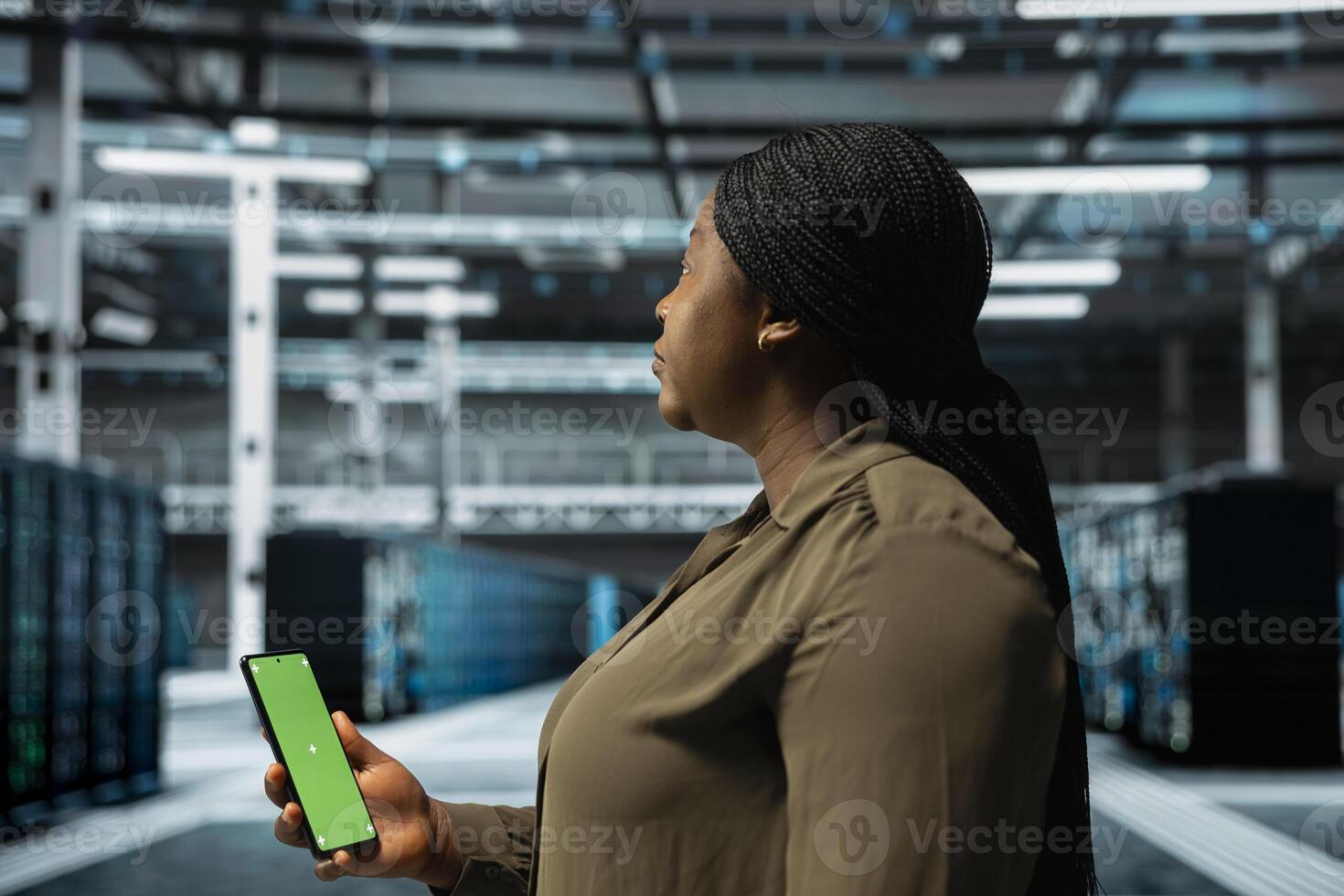 Woman in data center checking mainframes performance data on mockup smartphone. African american server farm worker using green screen phone to look at system alerts, monitoring equipment photo