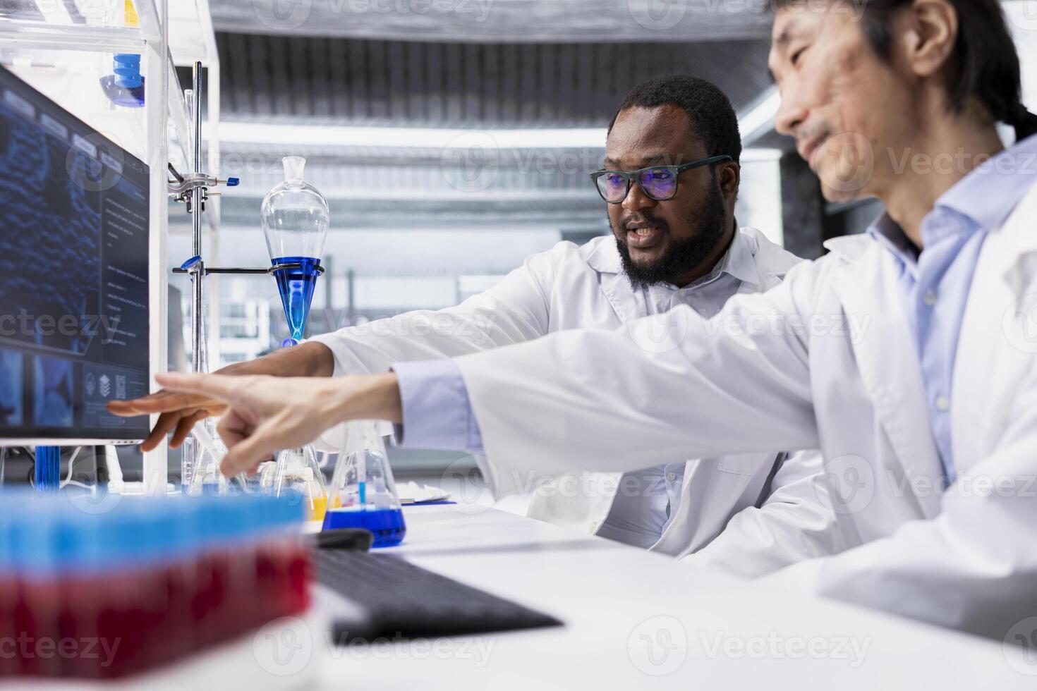 Team of biochemists in laboratory pointing to computer display, doing DNA data analysis. Research facility colleagues doing brainstorming using bioinformatics genomics software on PC in high tech lab photo
