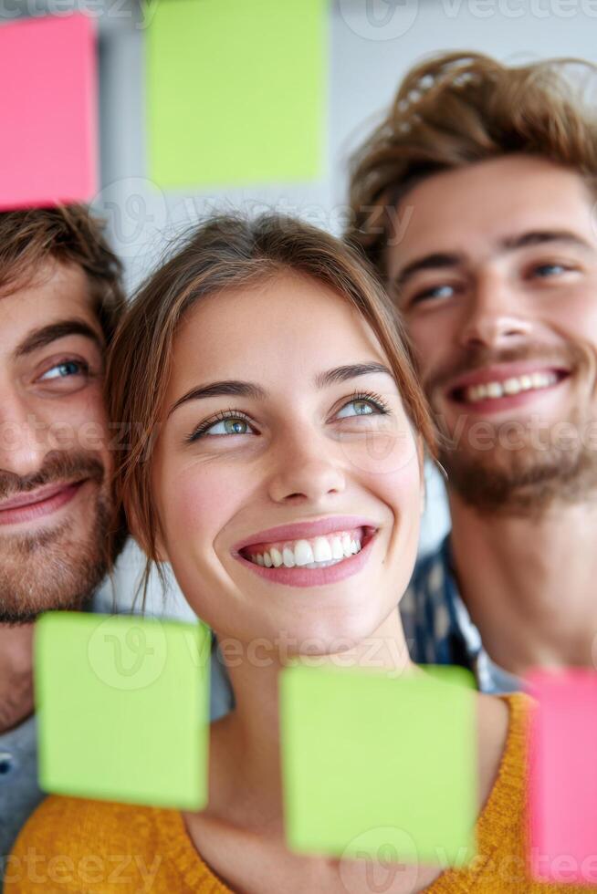 Smiling young woman with two men in background, brainstorming ideas with colorful sticky notes on wall, showcasing teamwork and creativity in a tech startup environment photo