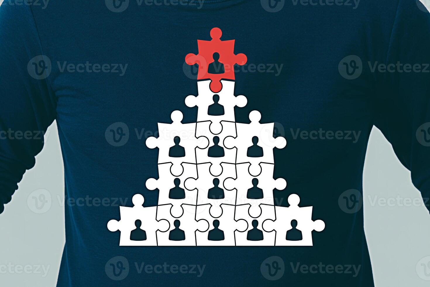 Person wearing a blue longsleeved shirt displaying a pyramid of puzzle pieces with a red piece at the apex symbolizing leadership and teamwork in a collaborative and hierarchical environment photo