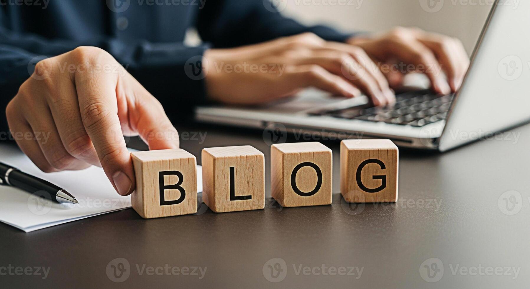 Focused professional arranging wooden blocks spelling BLOG on a desk while typing on a laptop conveying a sense of creativity online presence and the importance of digital content creation in modern b photo