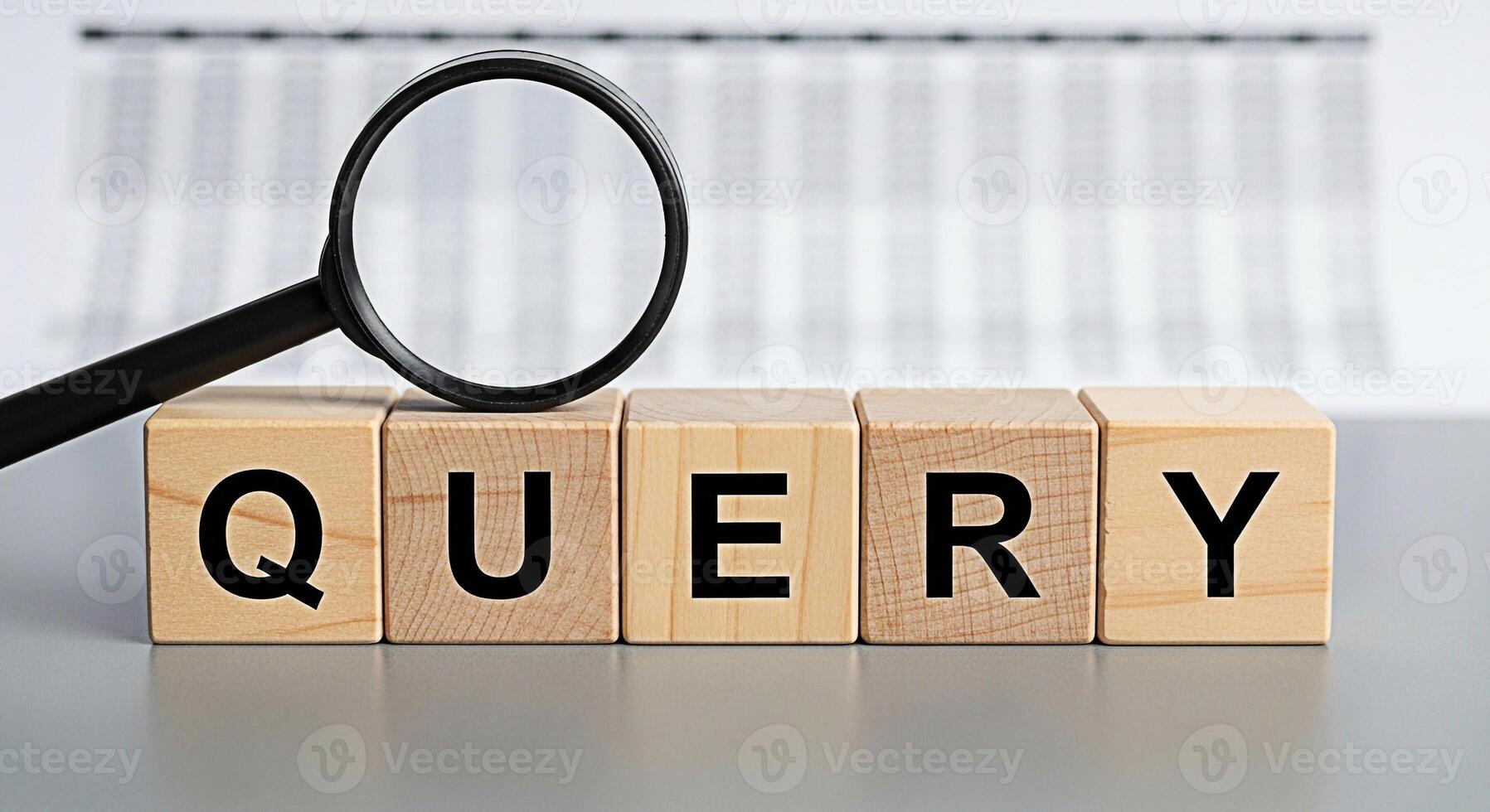 Magnifying glass analyzing the word QUERY spelled out on wooden blocks placed on a gray surface against a blurred spreadsheet background representing data analysis and information retrieval with a foc photo