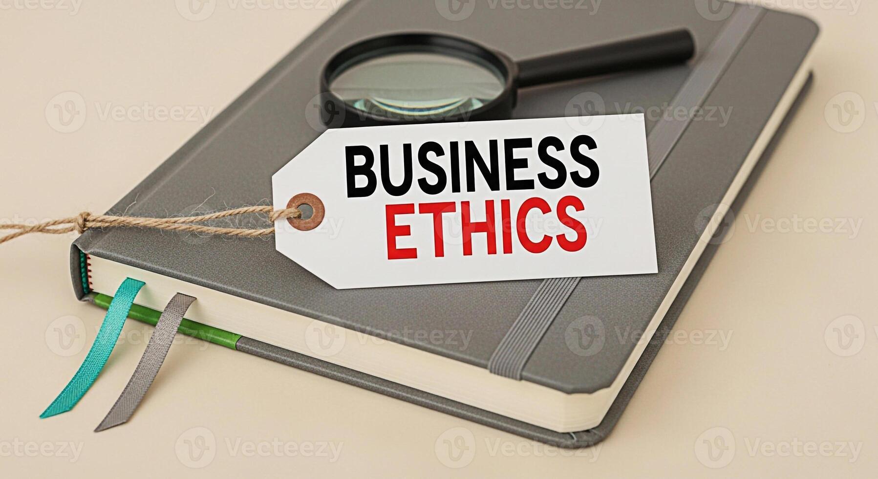 Magnifying glass resting on a closed notebook with a tag displaying Business Ethics in a neutral setting symbolizing corporate responsibility and the importance of ethical decisionmaking in the busine photo
