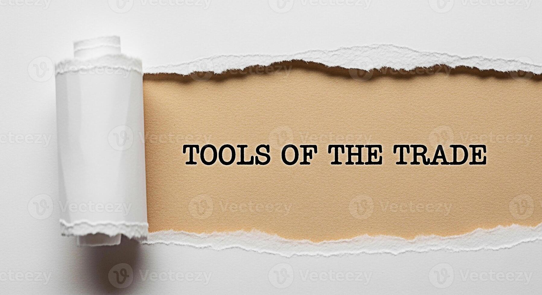 Torn paper revealing the phrase Tools of the Trade against a beige background symbolizing essential resources and expertise creating a sense of unveiling hidden knowledge and professional readiness photo