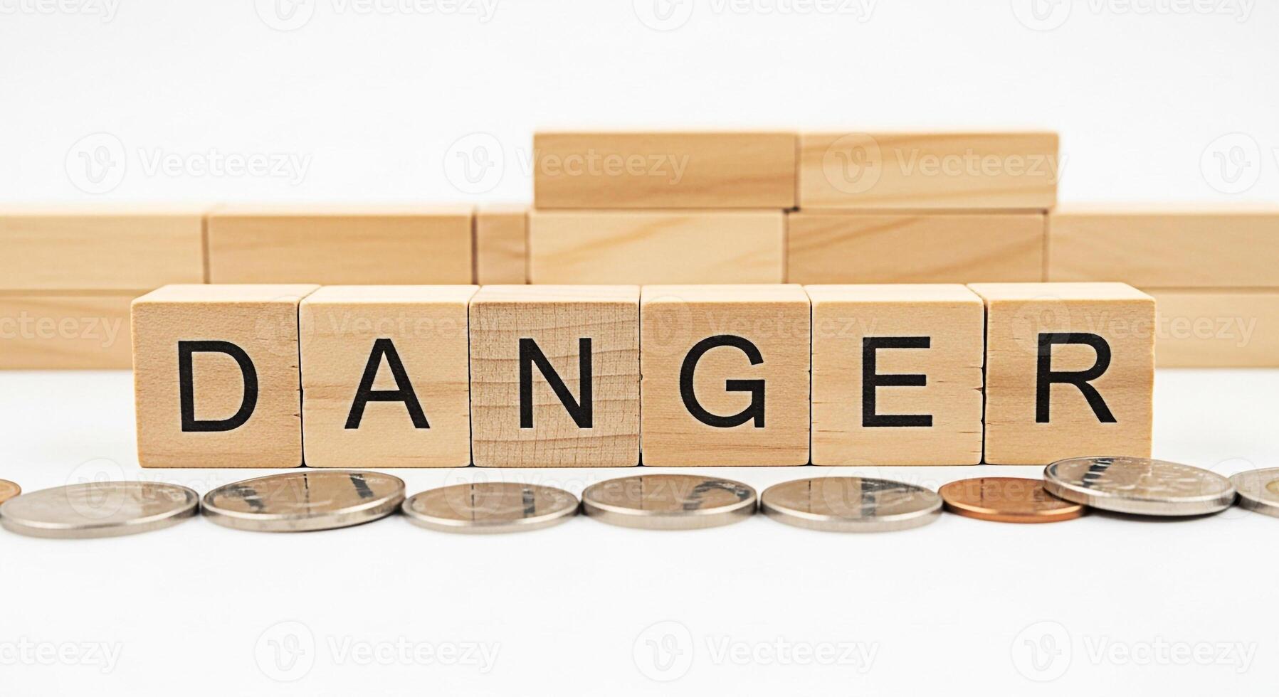 Wooden blocks spelling DANGER with coins scattered on a white surface representing financial risk and uncertainty in business creating a sense of caution and awareness about potential economic pitfall photo