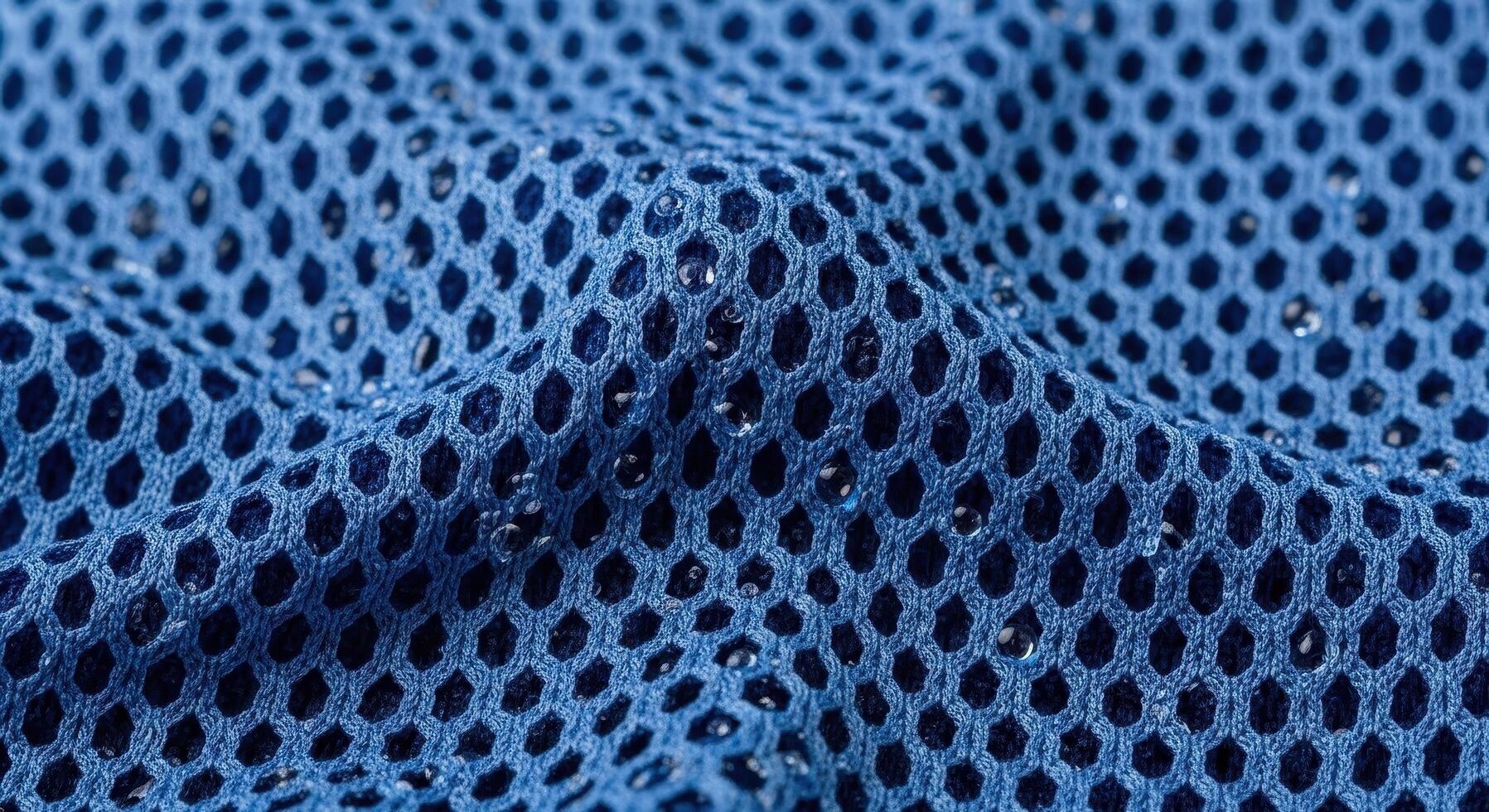 Close-up view of a vibrant blue mesh fabric texture with a pattern of hexagonal holes and water droplets, showcasing detail and design photo