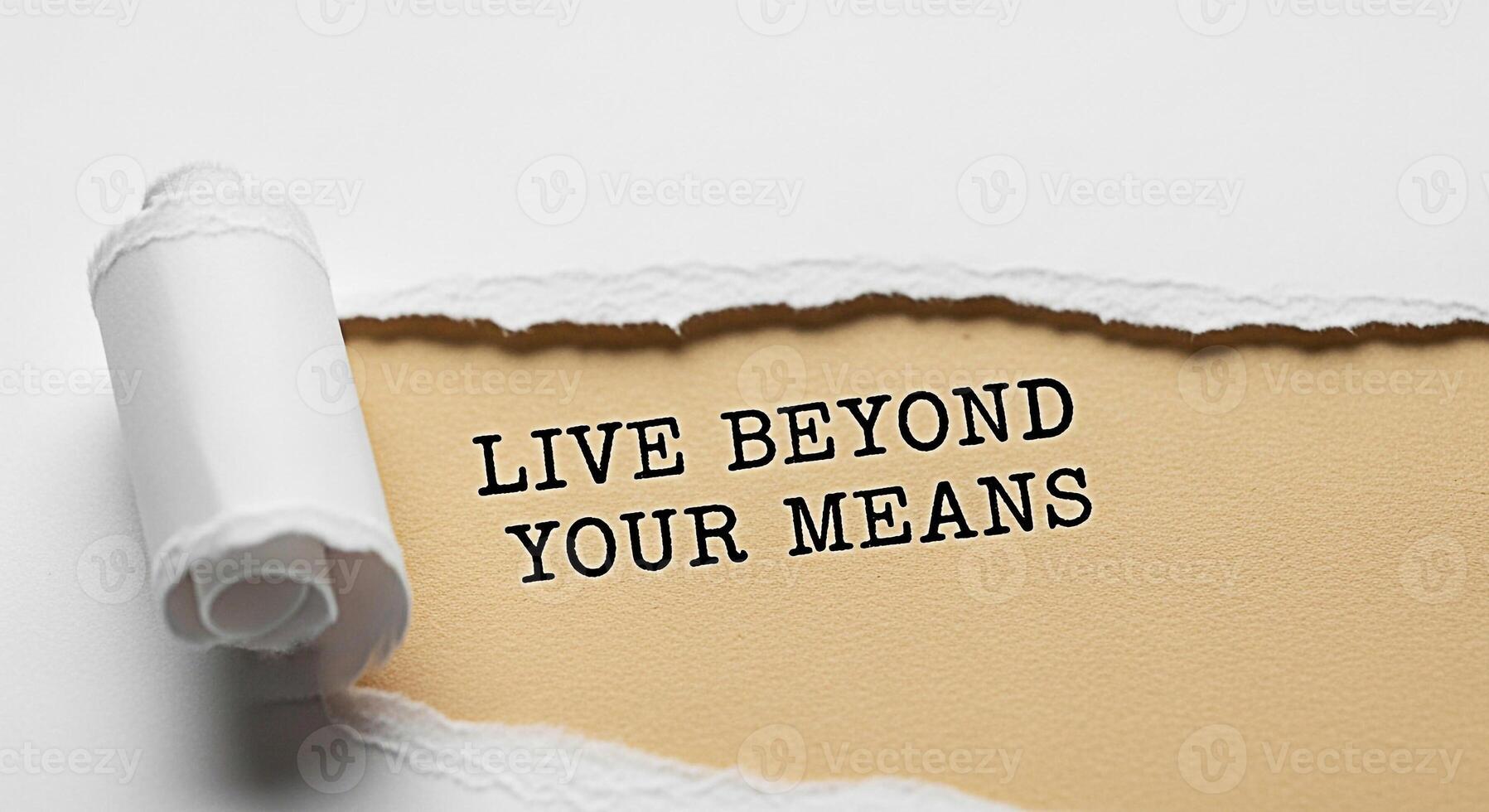 Torn paper revealing a message Live Beyond Your Means on a textured background representing financial risk overspending and the potential consequences of living beyond ones financial capabilities photo