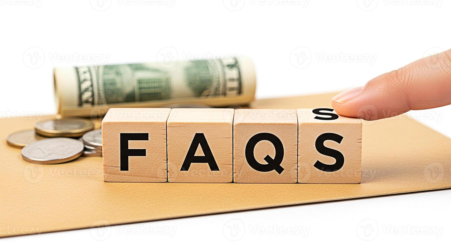 Closeup of wooden blocks spelling FAQs with a finger pointing set against a backdrop of money and coins on a brown surface conveying a sense of financial information and frequently asked questions photo