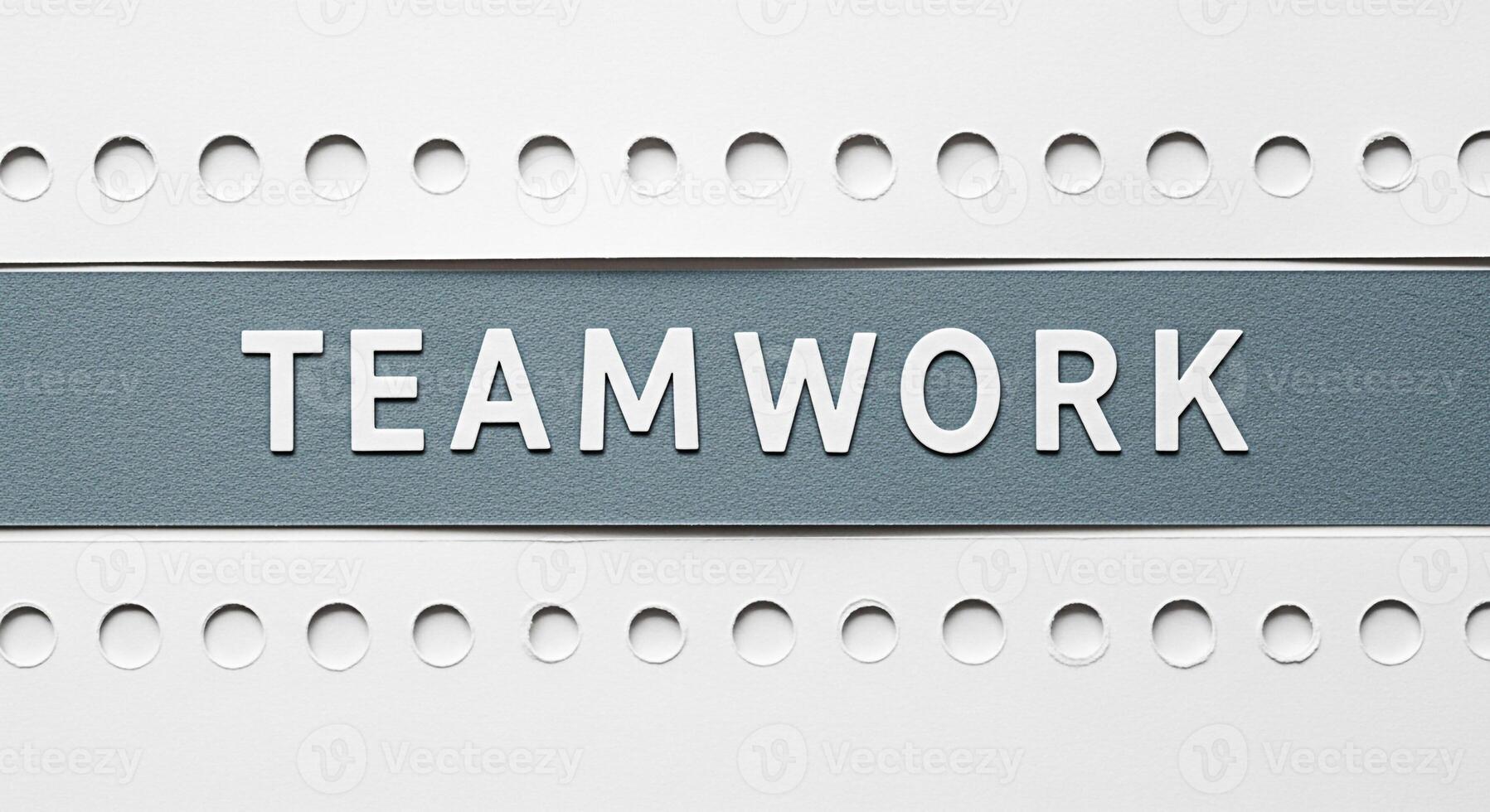 The word Teamwork displayed in white letters on a gray banner against a white background with decorative holes symbolizing collaboration and unity in a structured and organized environment promoting a photo