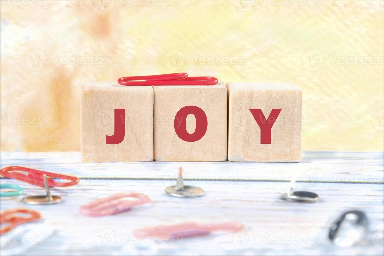 Wooden blocks display the word joy in bold red letters, surrounded by colorful paper clips on a light, softly colored surface, creating a cheerful atmosphere photo