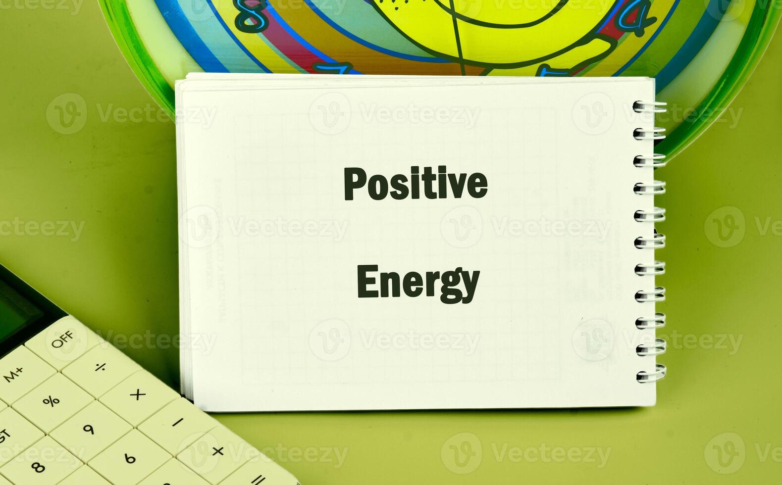 A spiral notebook opened to the words positive energy sits next to a calculator and colorful clock, symbolizing an encouraging atmosphere for growth and learning photo
