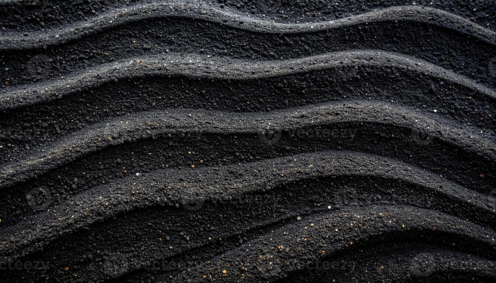 Black sand waves create a rhythmic pattern, displaying texture and form in an abstract natural background with subtle light and shadow play. photo