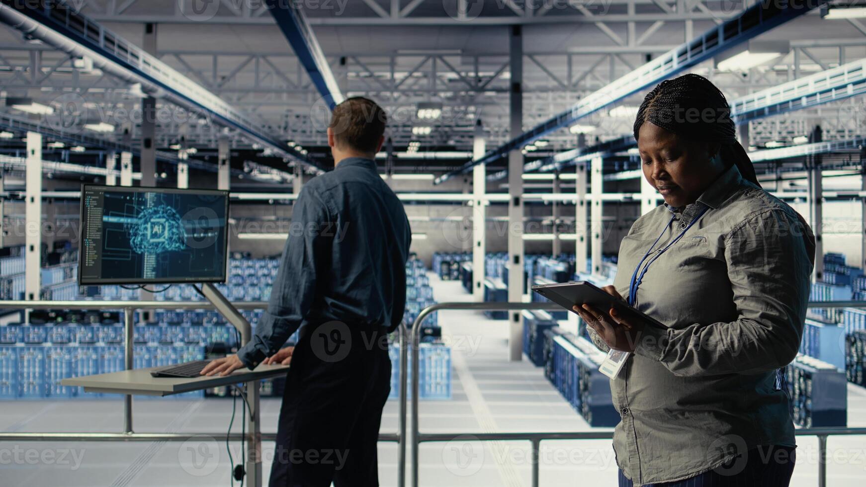 Team of data center technicians checks AI dashboard using laptop during systems review. Teamworking server hub colleagues test artificial intelligence tools on notebook, camera A photo
