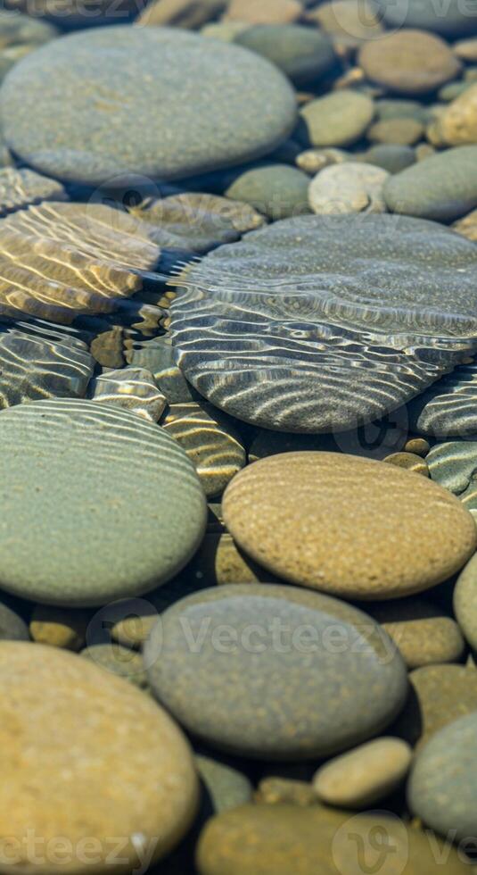 Smooth colorful river stones and pebbles submerged in clear shallow water creating a mesmerizing natural pattern and texture photo