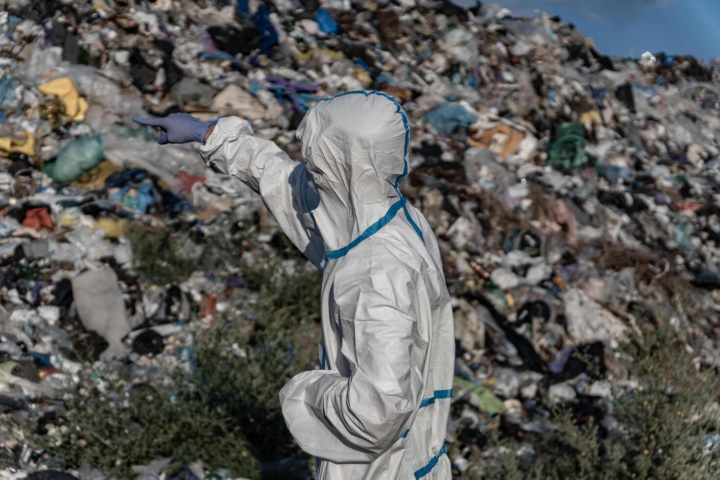 A worker in protective gear inspects a large landfill site filled with garbage and waste, showing the effects of pollution on the environment photo