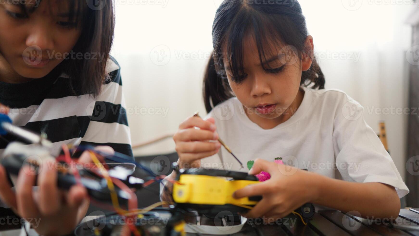 Two Asian girls working together on robotics project at home. Promoting STEM education, teamwork, coding, and problem-solving through hands on engineering and creative learning. photo