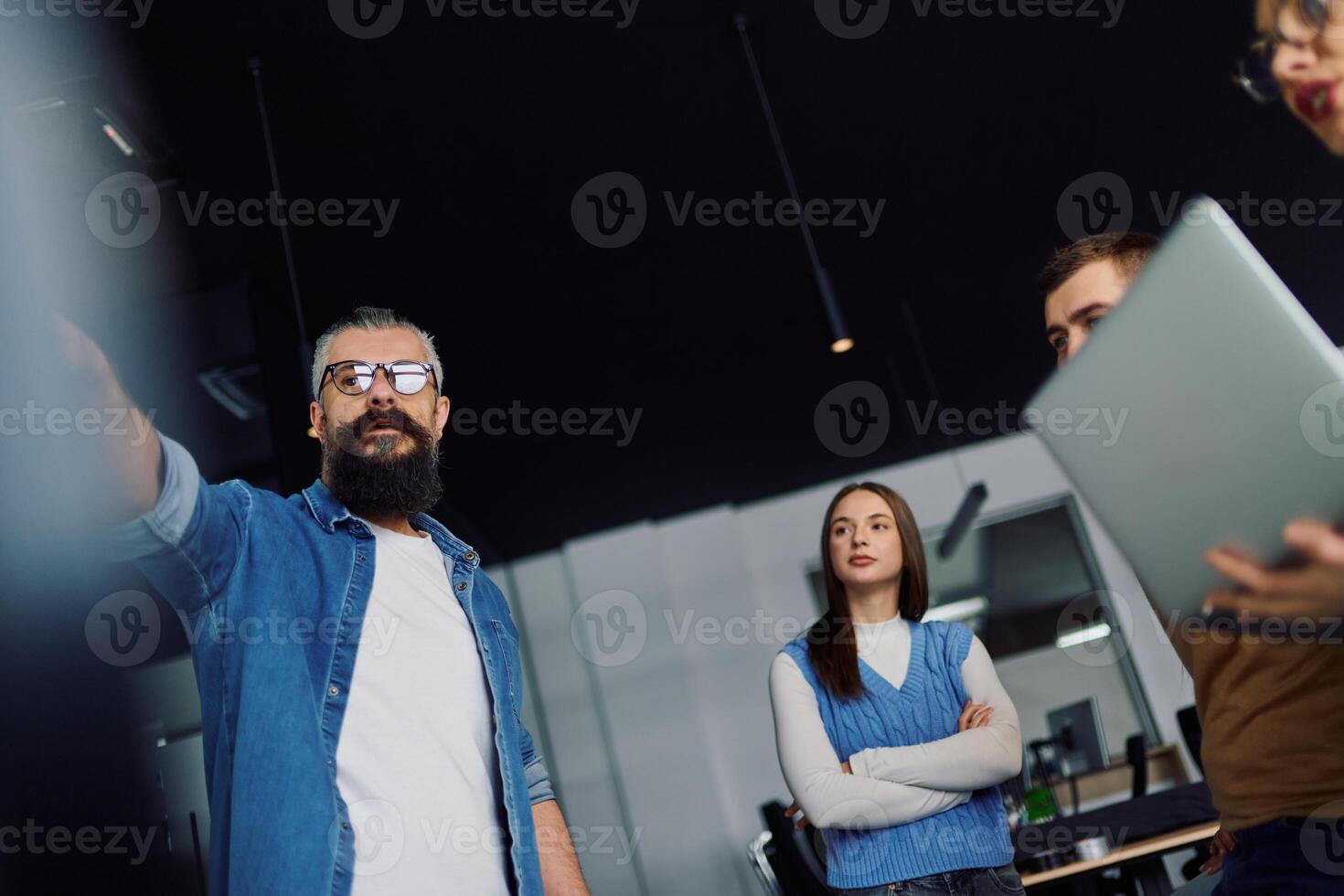 Group of young professionals gathered in a modern office for a business presentation. A man with a beard explains data charts on a large screen while the team listens attentively. Concept of teamwork photo