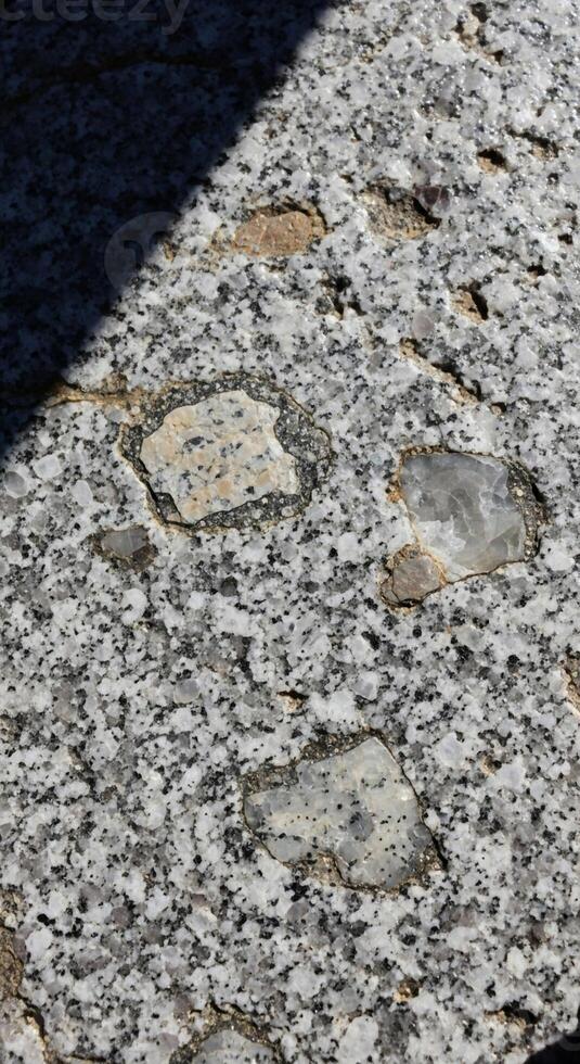 Close up view of a speckled granite surface with visible mineral inclusions and a diagonal shadow casting across it photo