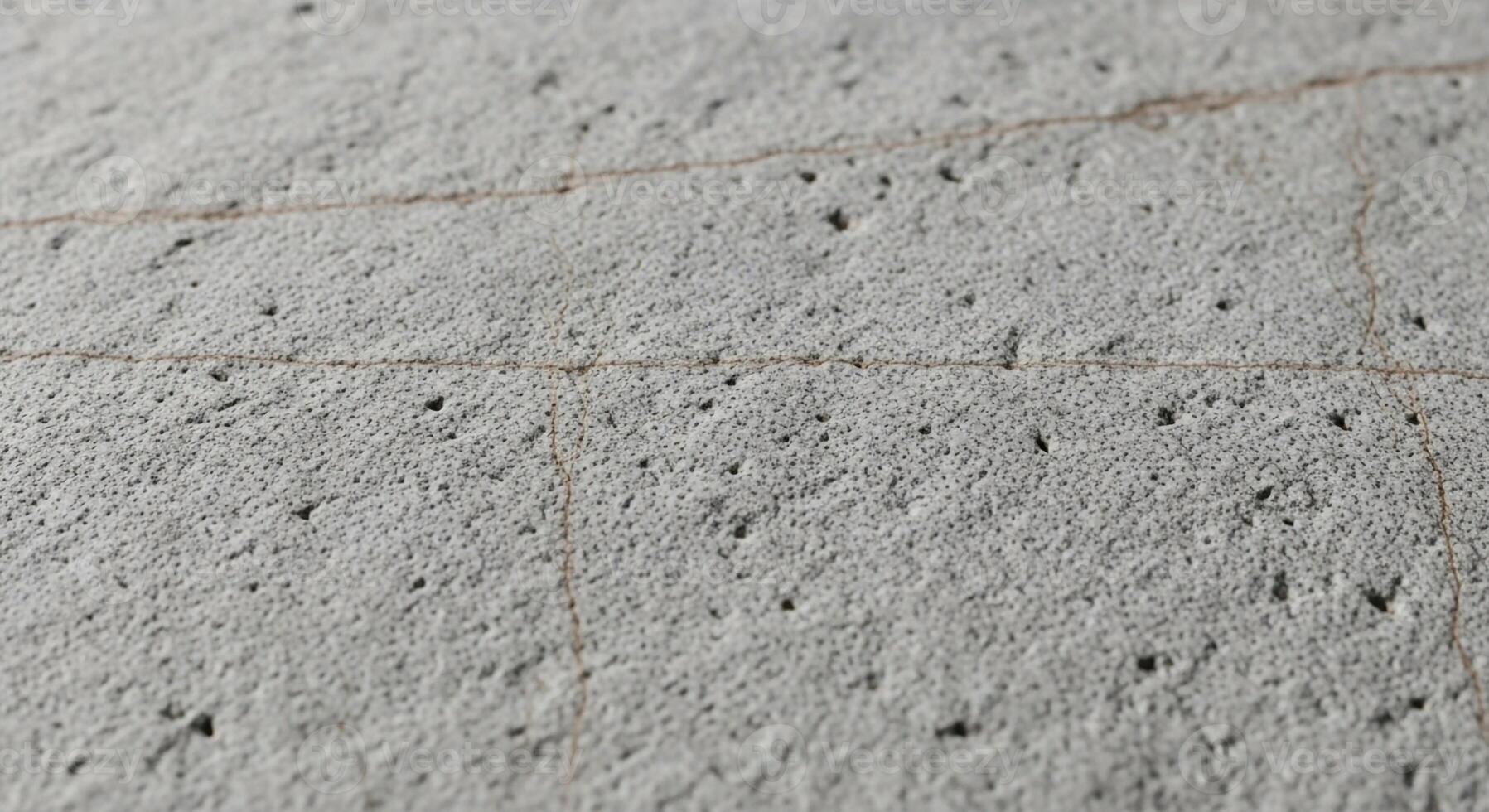 Close up textured surface of a light gray concrete wall with subtle yellow lines and small dark imperfections creating a rough abstract pattern photo