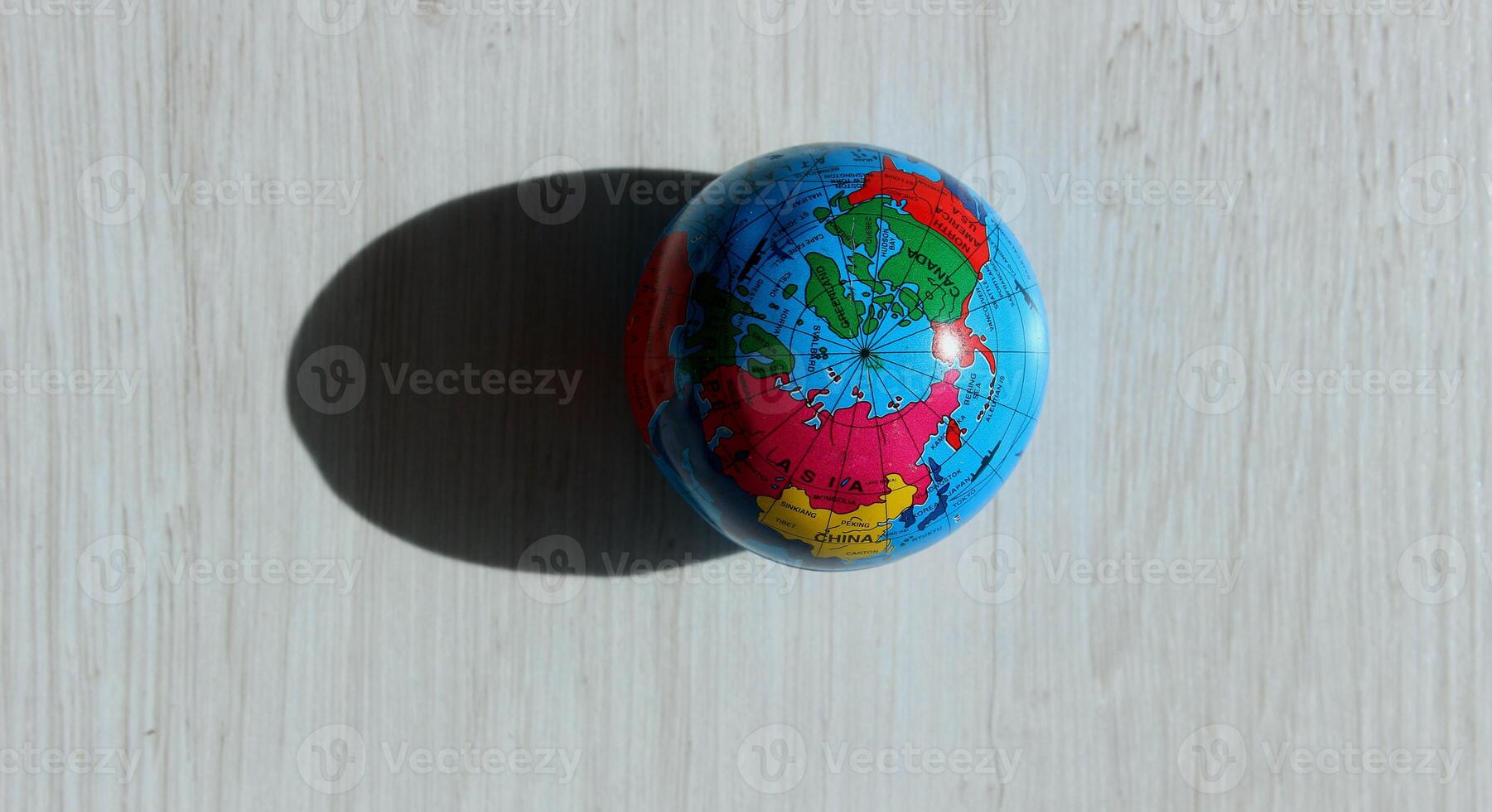 A top view of the North Pole on a colored globe that casts a textured shadow on a wooden surface. Conceptual photo illustrating different times of day on planet Earth