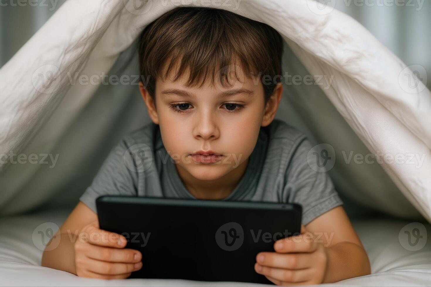 Young Child Using a Tablet Under a Blanket in a Cozy Indoor Setting With Shallow Depth Of Field, Emphasizing Focus on Screen photo