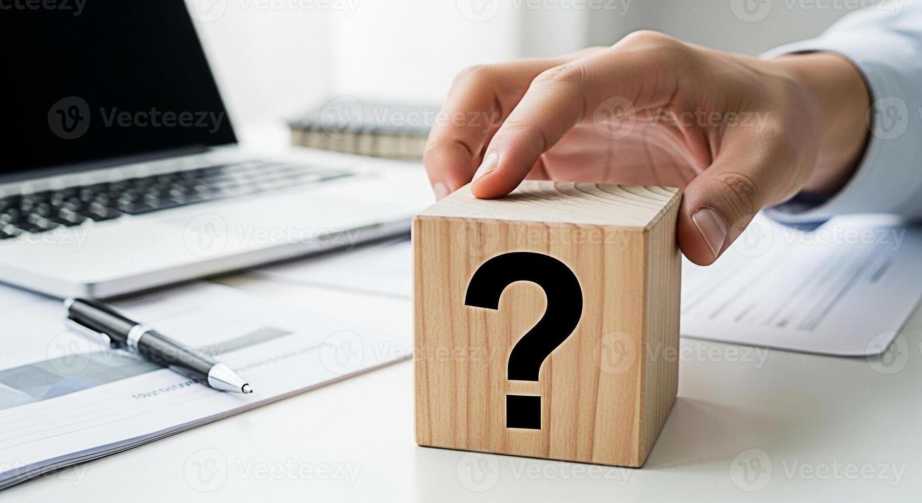 Hand placing a wooden block with a question mark on a white desk with a laptop pen and paperwork symbolizing uncertainty problemsolving and the need for answers in a professional setting photo