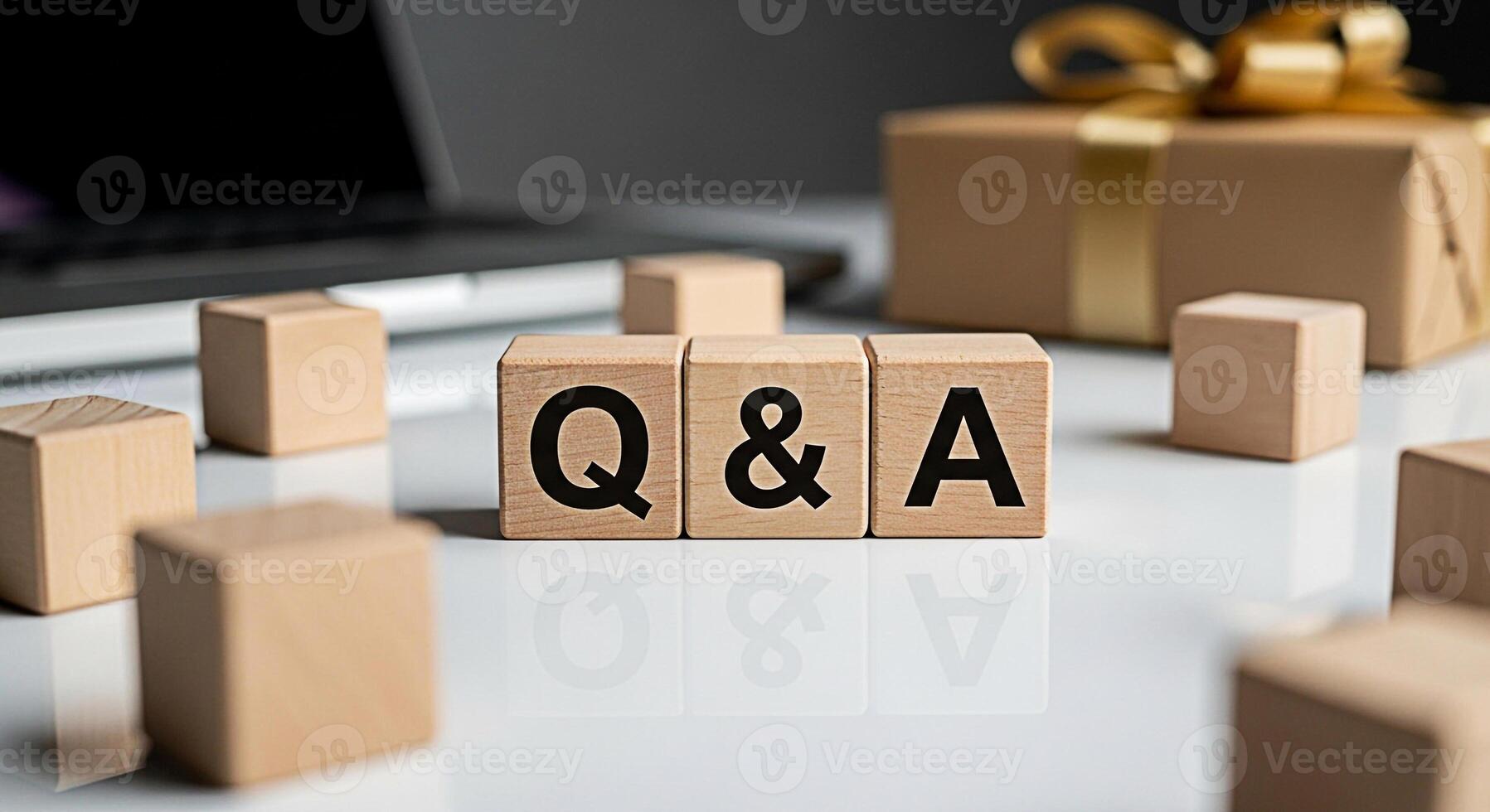 Wooden blocks displaying Q A on a reflective white surface with a laptop and gift box in the background representing knowledge sharing and customer support in a modern business setting photo