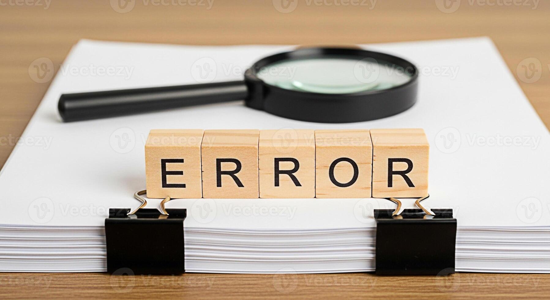 Wooden blocks spelling ERROR resting on a stack of white paper under a magnifying glass symbolizing mistakes and the need for careful review in business and documentation on a wooden desk photo