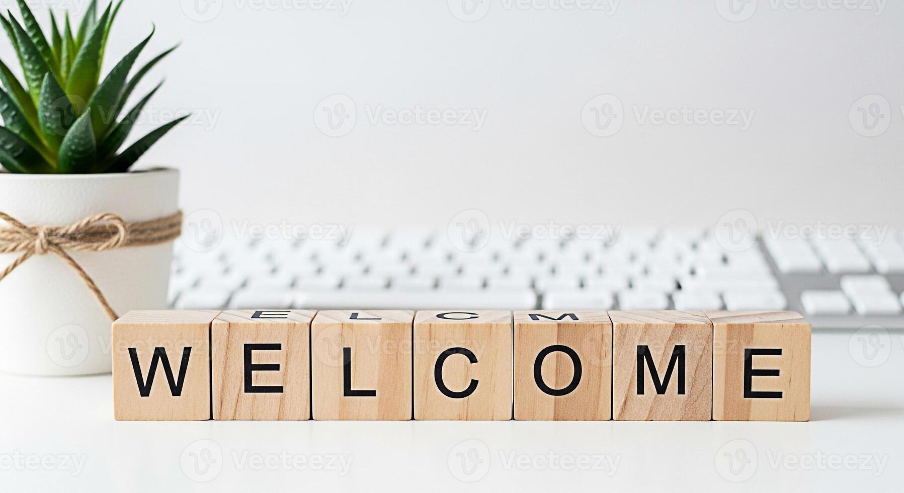 Wooden blocks spelling Welcome on a white desk next to a potted succulent plant and a computer keyboard creating a warm and inviting atmosphere for new beginnings and positive vibes photo