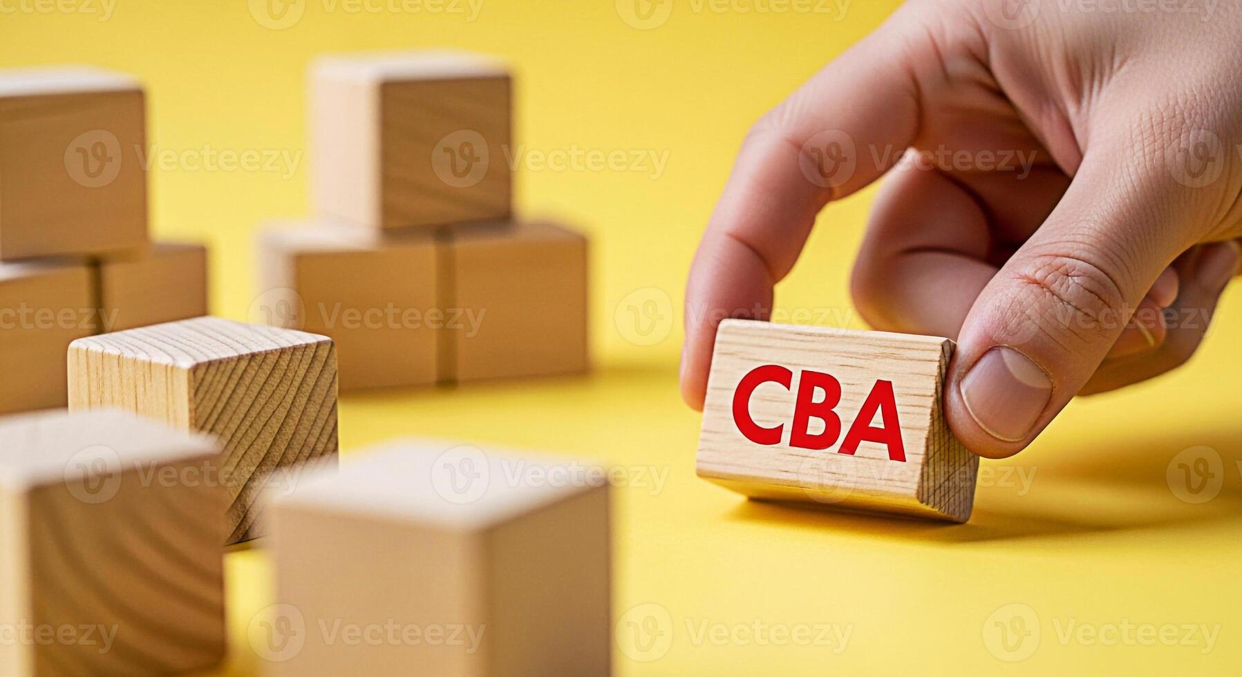 Hand placing a wooden block with the text CBA on a yellow surface symbolizing collective bargaining agreement and strategic business decisions with a focus on teamwork and collaboration photo