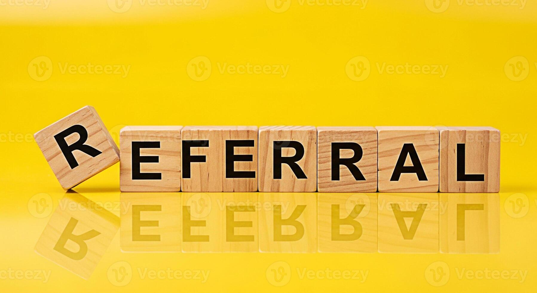 Wooden blocks spelling REFERRAL on a yellow reflective surface conveying a message of recommendation and business growth symbolizing trust and positive connections in a bright and optimistic setting photo