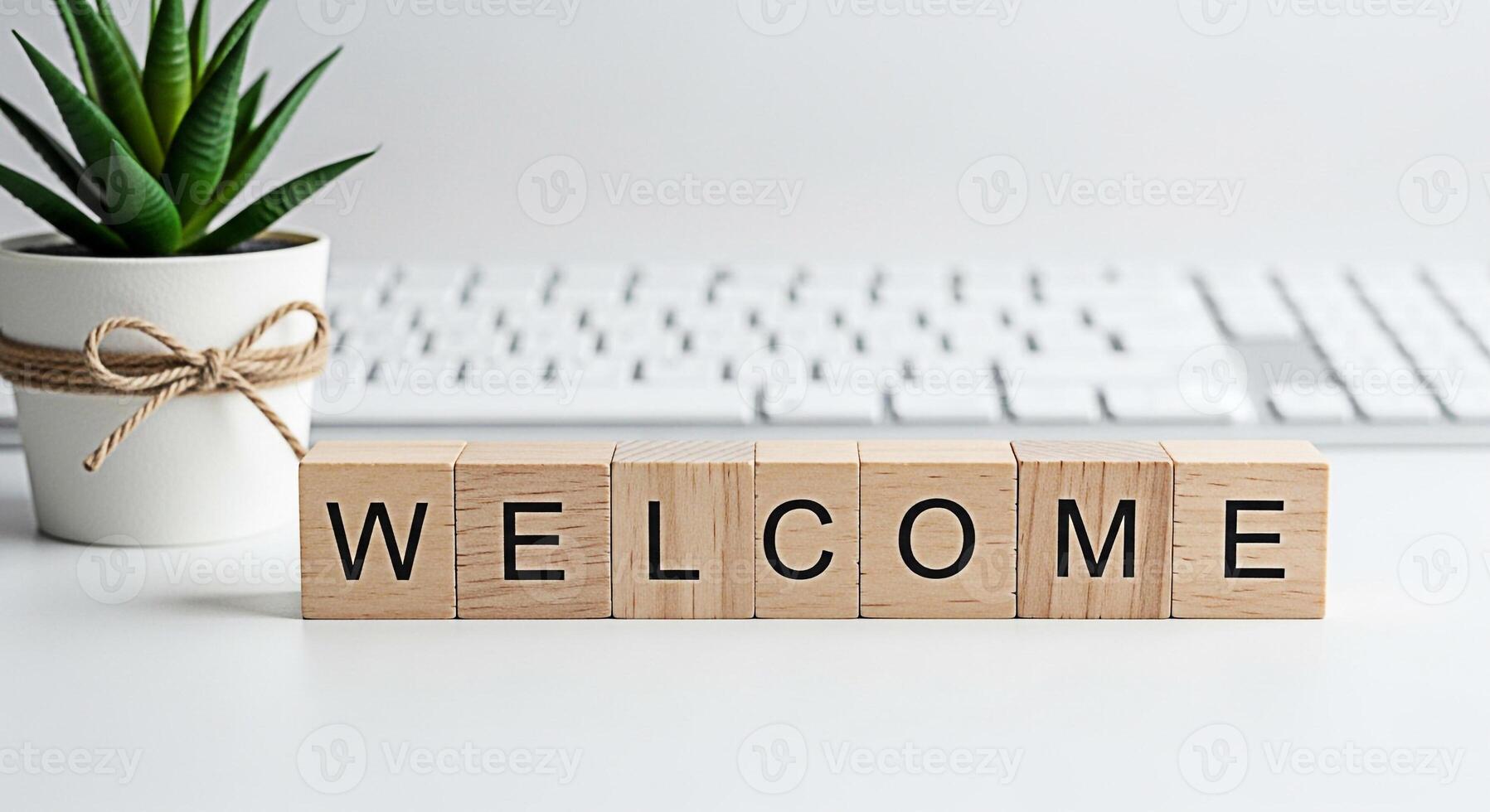 Wooden blocks spelling Welcome on a white desk next to a potted succulent plant and a computer keyboard creating a warm and inviting atmosphere for visitors and new beginnings photo