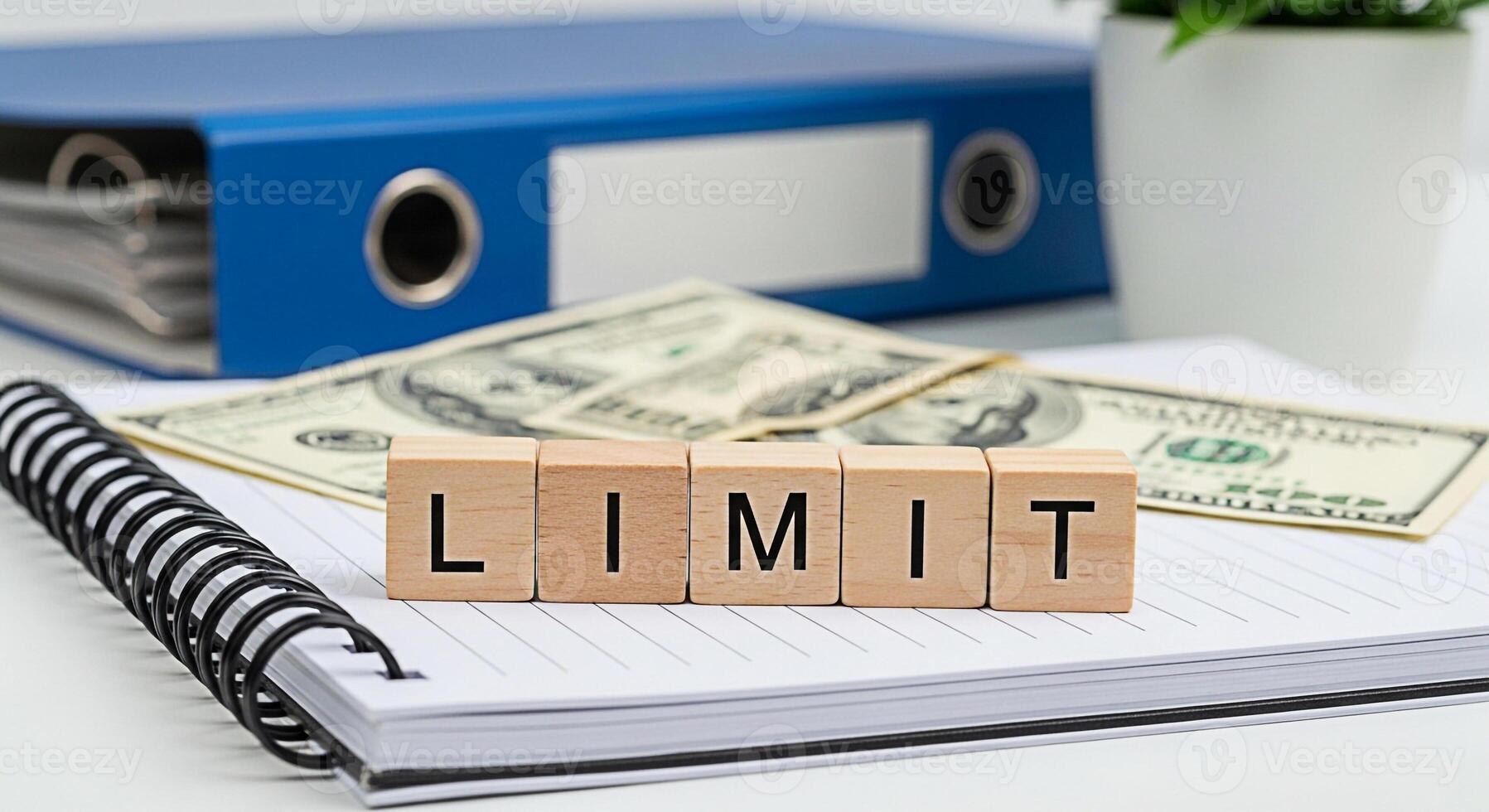 Wooden blocks spelling LIMIT resting on a notepad with money and a binder in the background representing financial constraints and budget management in a business office setting conveying a sense of c photo