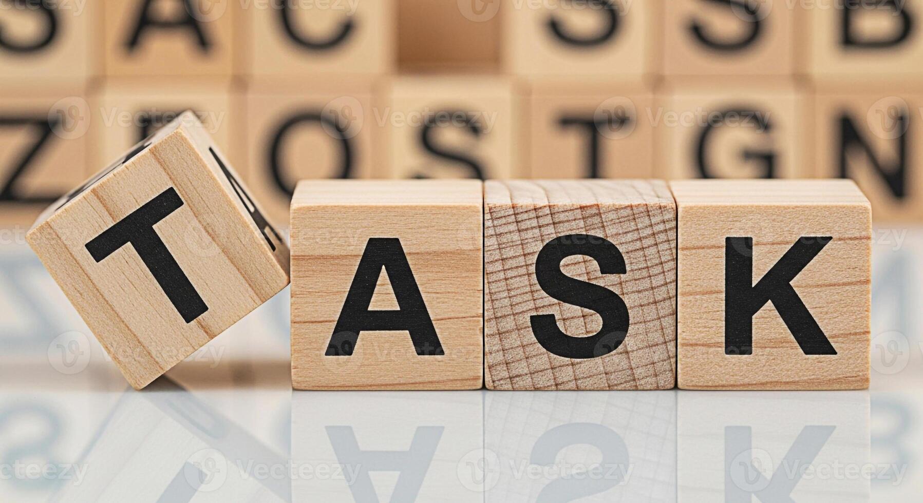 Wooden blocks spelling TASK on a reflective surface with a focus on project management and the importance of completing assignments in a timely and efficient manner to achieve success photo