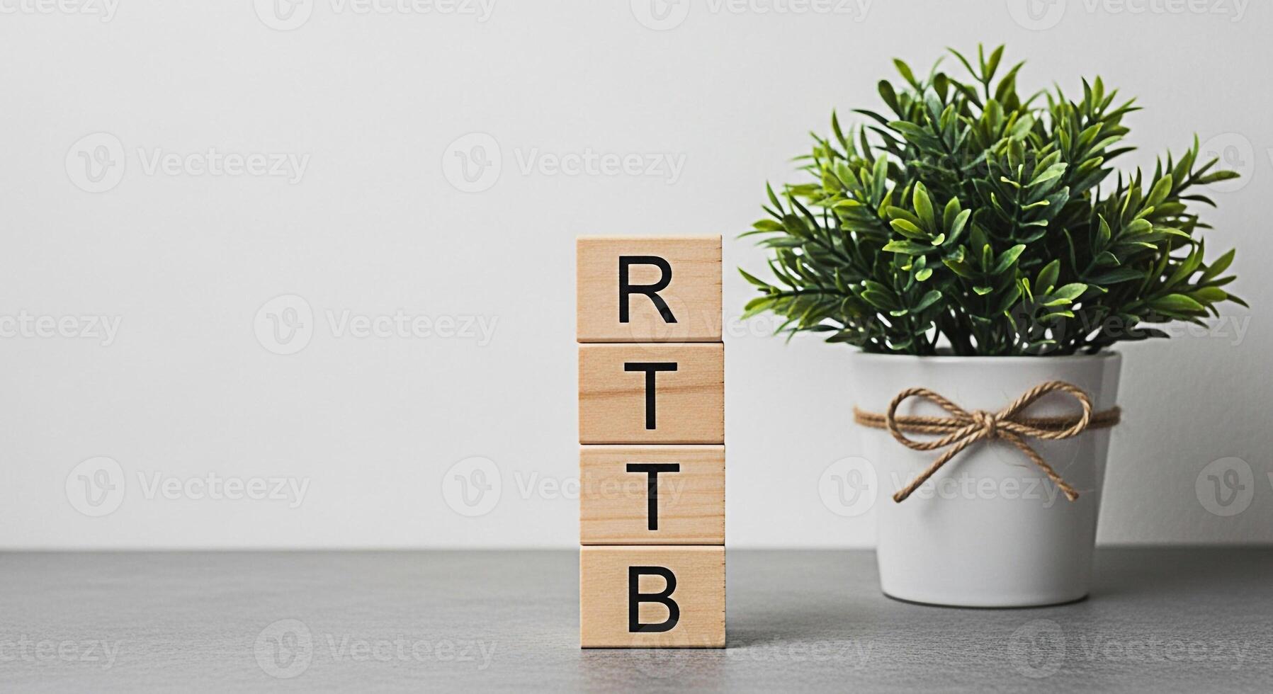 Wooden blocks displaying RTTB next to a potted plant on a gray surface against a white wall symbolizing a structured approach to growth and investment in a clean minimalist environment photo