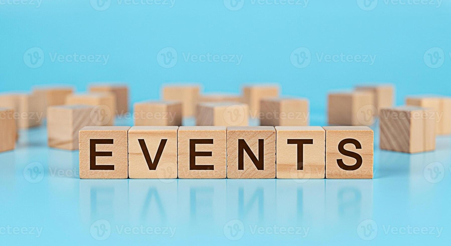 Wooden blocks spelling EVENTS on a reflective blue surface surrounded by other blocks symbolizing planning and organization for upcoming events and schedules in a bright and optimistic setting photo