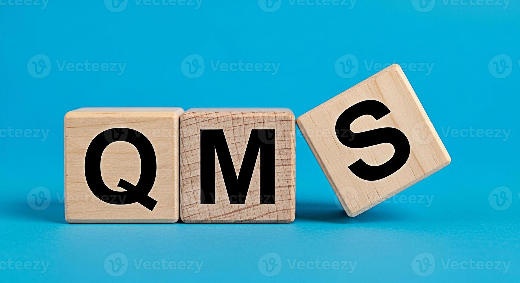 Wooden blocks displaying QMS on a blue surface representing quality management system implementation for continuous improvement and operational excellence in business and manufacturing processes photo